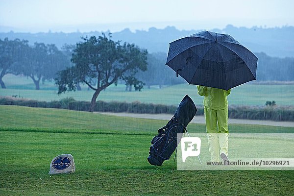 Rückansicht des Golfers neben der Golftasche im Regenschirm