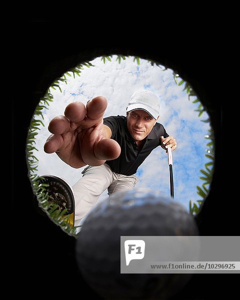 Blick durch das Loch des Golfers  der nach dem Golfball greift
