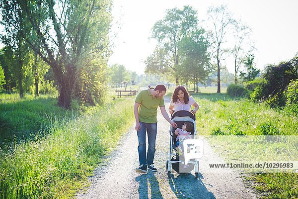 Mittleres erwachsenes Paar mit Kleinkind Tochter im Kinderwagen beim Spaziergang im Park