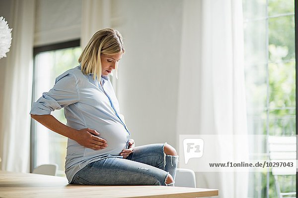 Vollzeitschwangerschaft junge Frau auf dem Küchentisch sitzend