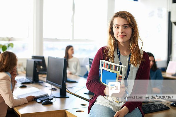 Porträt einer Studentin  die eine Datei vor der Computerklasse hält