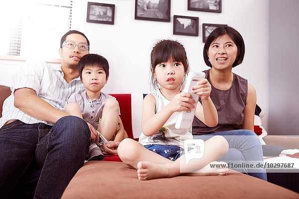 Junge moderne chinesische Familie von Eltern und zwei kleinen Kindern die gemeinsam zu Hause auf dem Sofa sitzen und fernsehen.