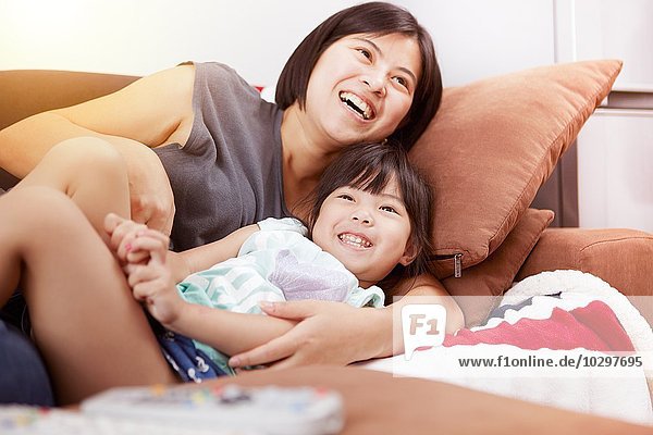 Young Chinese mother and daughter laying on sofa watching the television together at home