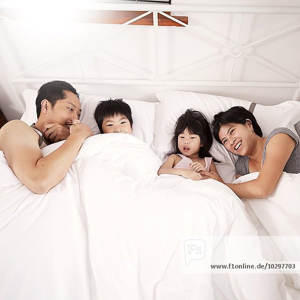 Junge chinesische Elternfamilie und zwei kleine Kinder  die zu Hause zusammen im Bett liegen