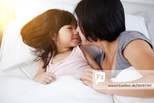 Young Chinese mother and daughter laying in bed together at home