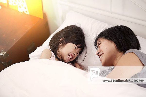 Junge chinesische Mutter und Tochter liegen zusammen zu Hause im Bett.