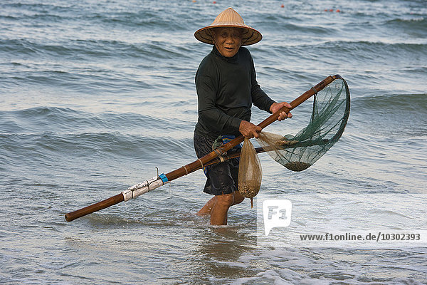 Mussel hunter  shellfish fisherman wearing a straw hat  Cua Dai beach in Hoi An  Vietnam  Asia
