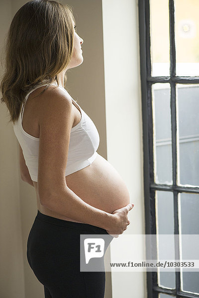 Pregnant woman looking out window contemplatively