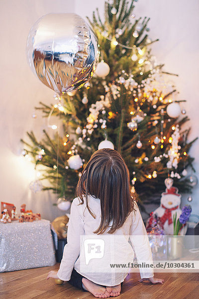Mädchen sitzt auf dem Boden und starrt auf den Weihnachtsbaum.