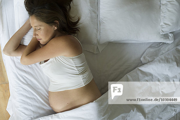 Eine schwangere Frau schläft allein im Bett.