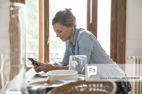 Junge Frau mit Smartphone in der Küche