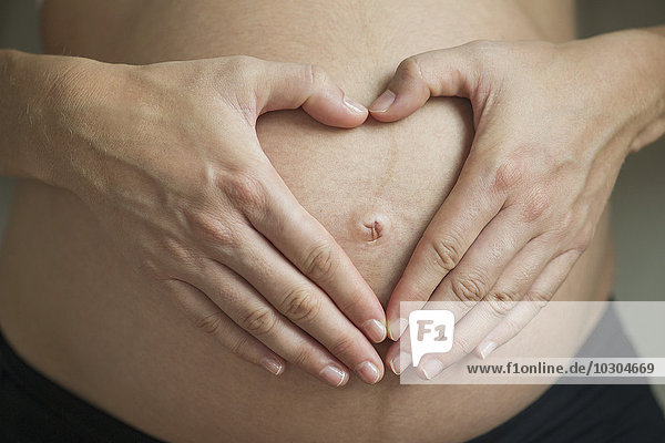 Schwangere Frau macht Herzform mit Händen um den Bauchnabel herum