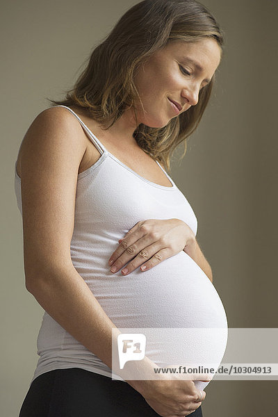 Eine schwangere Frau  die mit Zuneigung auf ihren Bauch blickt.