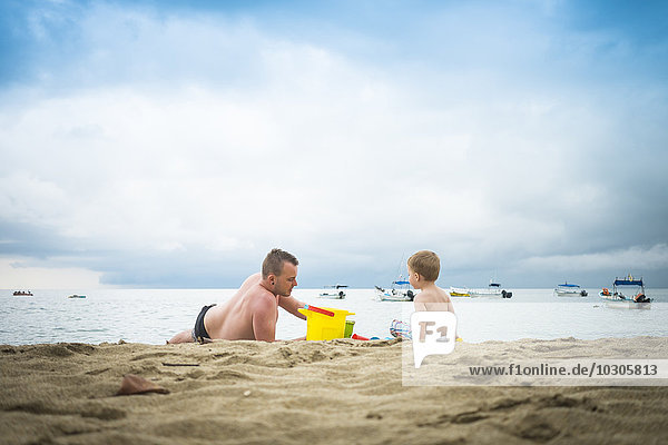 Mexiko  Vater spielt mit seinem kleinen Sohn im Sand an einem Strand.