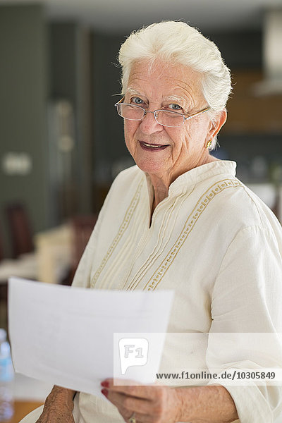 Porträt einer lächelnden Seniorin mit Brille  die ein Blatt Papier hält.