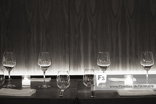 Mit Weingläsern  Servietten und Kerzen gedeckter Tisch in einem Stadtrestaurant. Schwarz-Weiß-Bild.