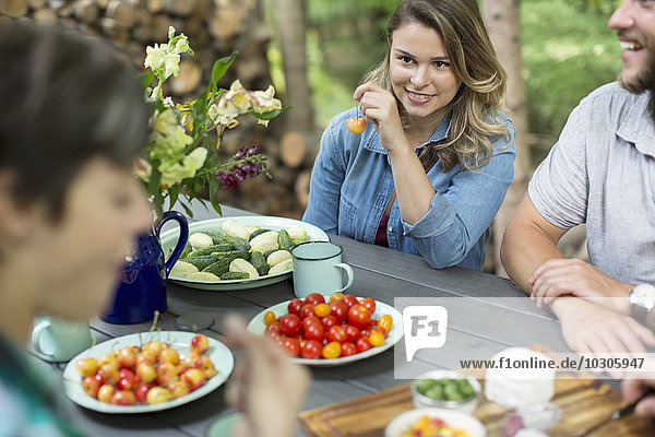 Drei Personen saßen an einem Tisch im Freien  mit frischem Obst und Gemüse in Tellern auf dem Tisch.