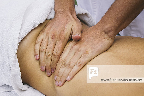 Hände einer Physiotherapeutin  die den Rücken einer Frau massiert.