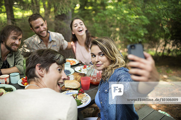 Ein Picknick im Wald. Freunde sitzen um einen Tisch herum  eine Frau nimmt sich der Gruppe an.