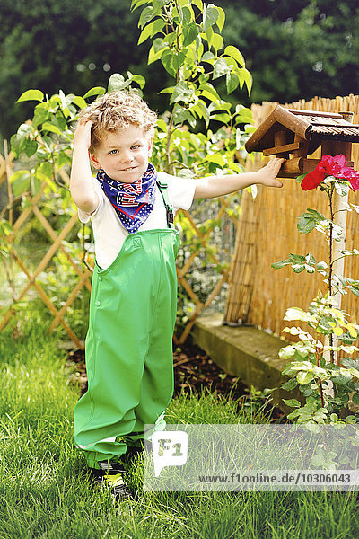Porträt des kleinen Jungen in grüner Latzhose im Garten stehend