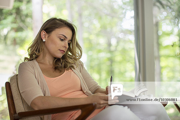Eine sitzende Frau hält ein offenes Tagebuch und einen Stift in der Hand.