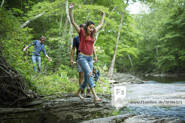 Zwei Männer und zwei Frauen am Flussufer  eine springt über Trittsteine.