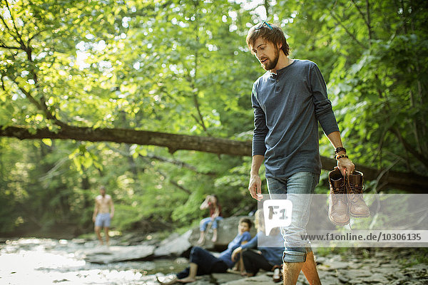 Ein Mann  der seine Stiefel trägt und auf den Felsen an einem Fluss läuft.