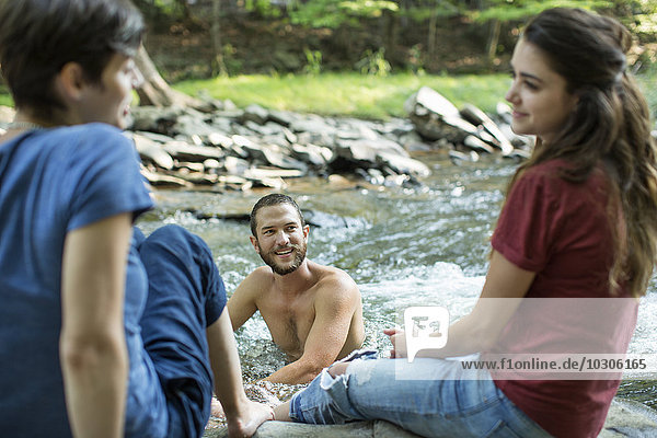 Ein Mann im Fluss und zwei Frauen am Flussufer sitzend.