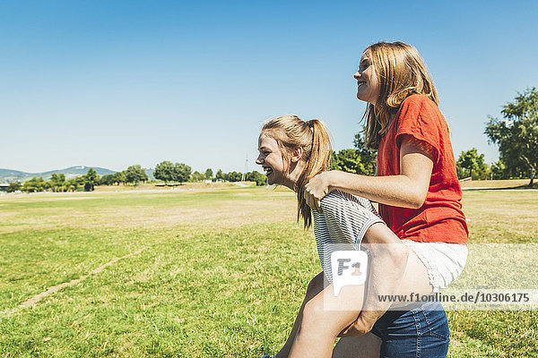 Carefree teenage girl carrying friend piggyback in park
