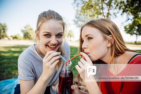 Zwei Teenager-Mädchen teilen sich einen Eistee im Park.