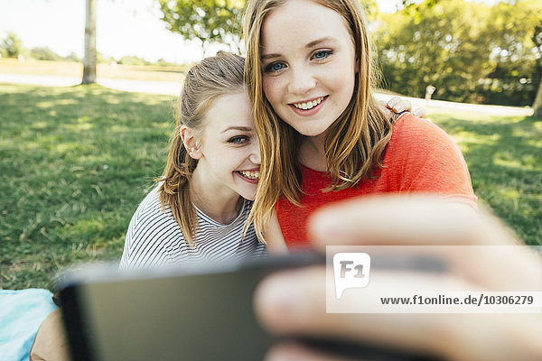 Zwei fröhliche Teenager-Mädchen mit einem Selfie auf der Wiese