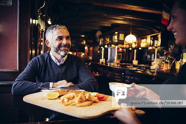 Smiling man in restaurant receiving Wiener Schnitzel with French fries