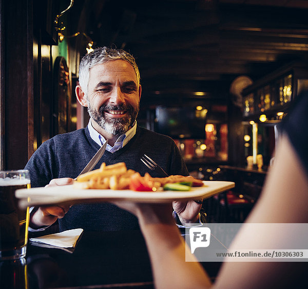 Smiling man in restaurant receiving Wiener Schnitzel with French fries