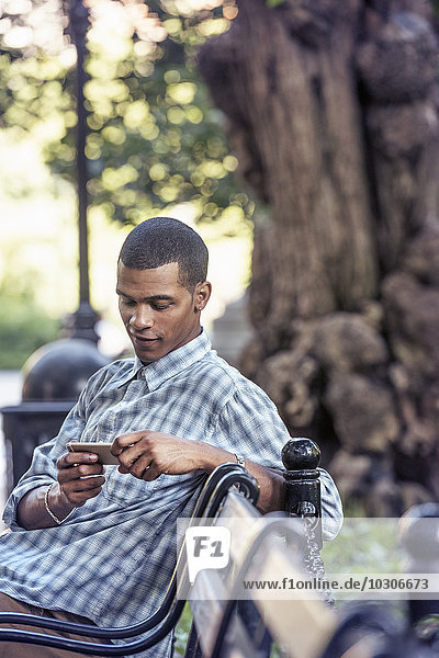 Ein Mann  der mit seinem Smartphone auf einer Parkbank sitzt