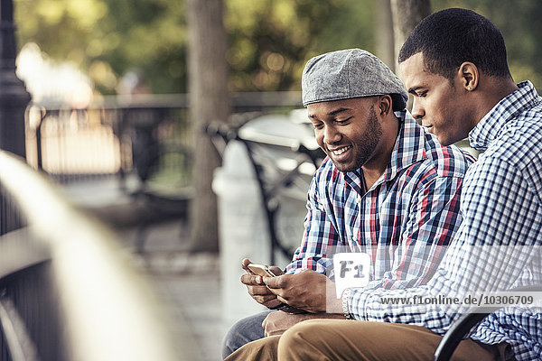 Two men sitting in a park  looking at a smart phone