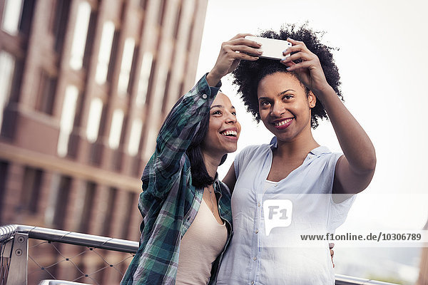 Zwei Frauen  die vor einem großen Gebäude in der Stadt posieren und ein Selfie machen