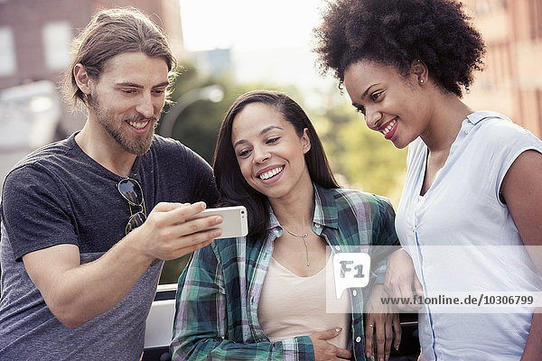 Ein Mann und zwei Frauen schauen auf ein Smartphone
