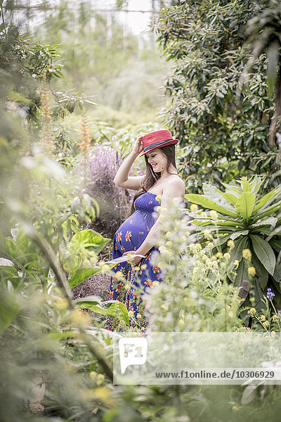 Porträt einer schwangeren Frau mit rotem Hut im Gewächshaus