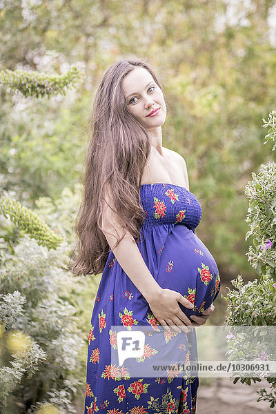 Portrait of pregnant woman wearing summer dress standing in a greenhouse