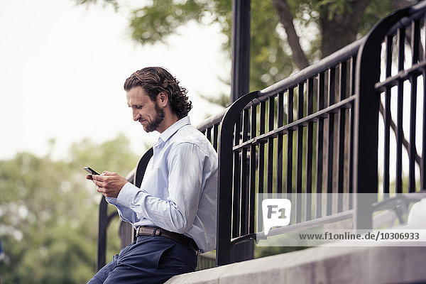 Ein Mann hält auf der Straße inne  sitzt auf einer Stufe und überprüft sein Handy.