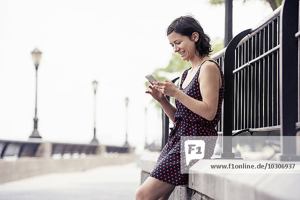 Eine Frau  die auf einer Straße eine Pause macht  sitzt und ihr Handy überprüft.