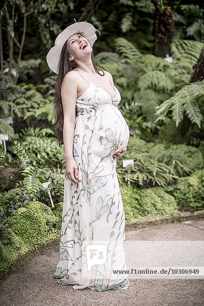 Porträt einer schwangeren Frau mit Sommerkleid und Hut im Gewächshaus