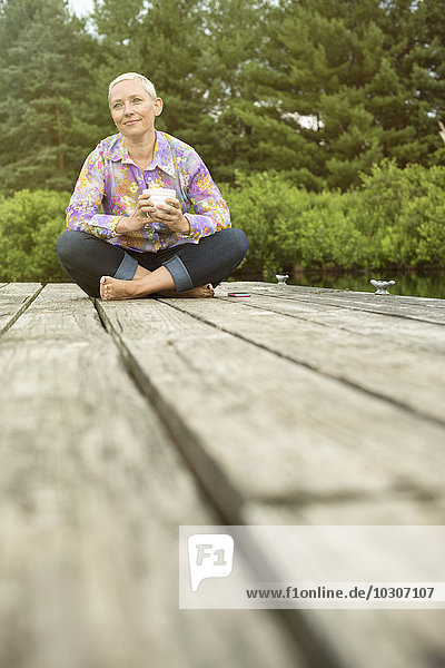 A woman sitting outdoors on a dock with a cup of coffee