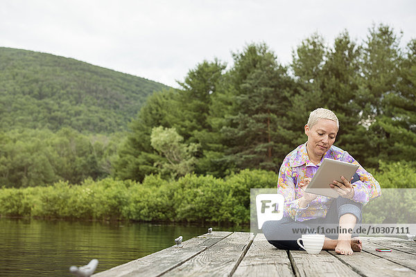 Eine Frau sitzt im Freien auf einem Steg und benutzt ein digitales Tablett.