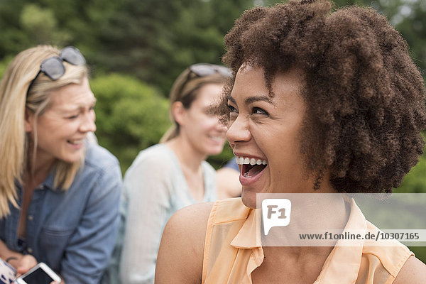 Eine Frau in einer Gruppe von Freunden im Freien beim Lachen.