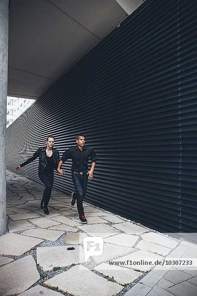 Black dressed young couple running hand in hand in front of black facade