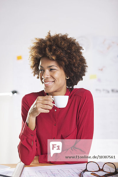 Portrait of smiling young female architect drinking coffee at her desk