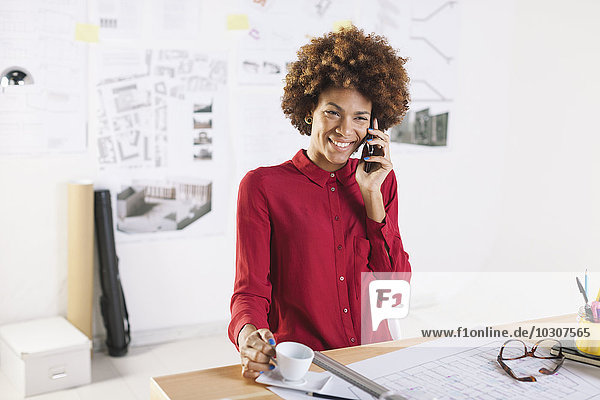 Portrait of smiling young female architect telephoning with smartphone at her office