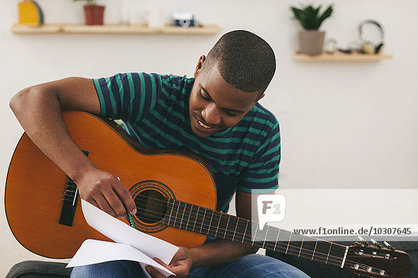 Lächelnder Mann mit Gitarre  der etwas aufschreibt.