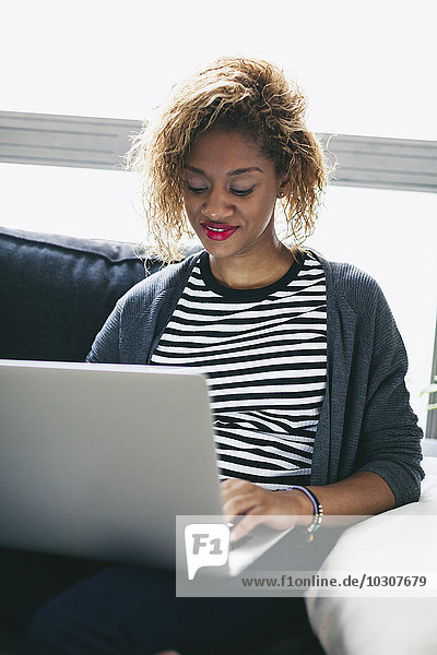 Young woman sitting on the couch using laptop